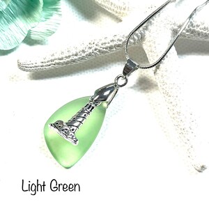 May include: A silver chain necklace with a light green glass pendant shaped like a lighthouse. The pendant has a silver lighthouse design.