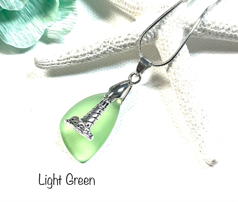May include: A silver chain necklace with a light green glass pendant shaped like a lighthouse. The pendant has a silver lighthouse design.