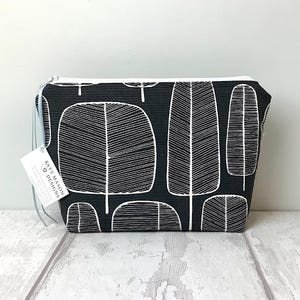 Op de afbeelding: Zwarte en witte toilettas met een herhalend patroon van gestileerde bomen. De tas heeft een witte rits en een wit label met de tekst "Katy Mason Designs".