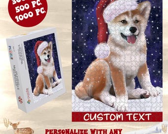 May include: A jigsaw puzzle featuring an Akita dog wearing a red and white Santa hat against a dark blue snowy background. The box displays the same image with the text "THE WORLD'S MOST BEAUTIFUL JIGSAW PUZZLES" and "300 PC. 500 PC. 1000 PC."