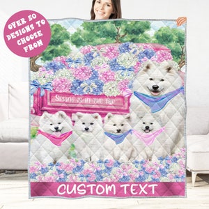 May include: A white quilted blanket featuring a graphic of five Samoyed dogs with bandanas, a pink truck filled with blue and pink flowers, and the text "Spring is in the Air". The blanket has the text "Custom Text" at the bottom.