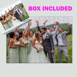 Puede incluir: Un rompecabezas de 1000 piezas con una foto de boda. La imagen muestra a una novia y un novio con su grupo de boda, todos sonriendo y celebrando. La caja del rompecabezas es visible, con el texto "BOX INCLUDED".