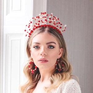 May include: A woman wearing a white lace dress with a red beaded crown and matching earrings.