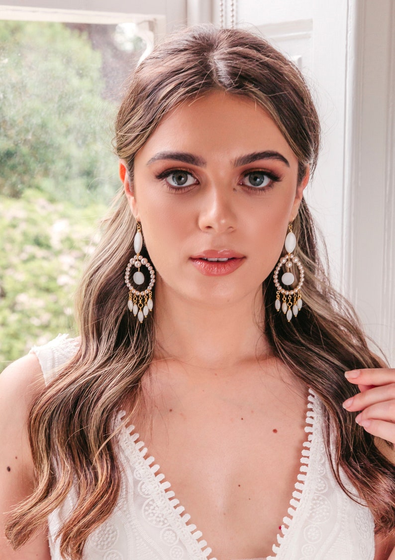May include: Elegant chandelier earrings with a pearl and gold design. The earrings feature a large oval pearl at the top, a circle of small pearls, and dangling teardrop-shaped pearls. The earrings are a beautiful accessory for special occasions.