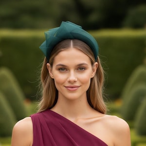 May include: A dark green headband featuring a structured, layered tulle accent on one side. The accessory is worn on the head, showcasing a smooth, solid-coloured band base that transitions into a voluminous, pleated fabric detail made of sheer material.