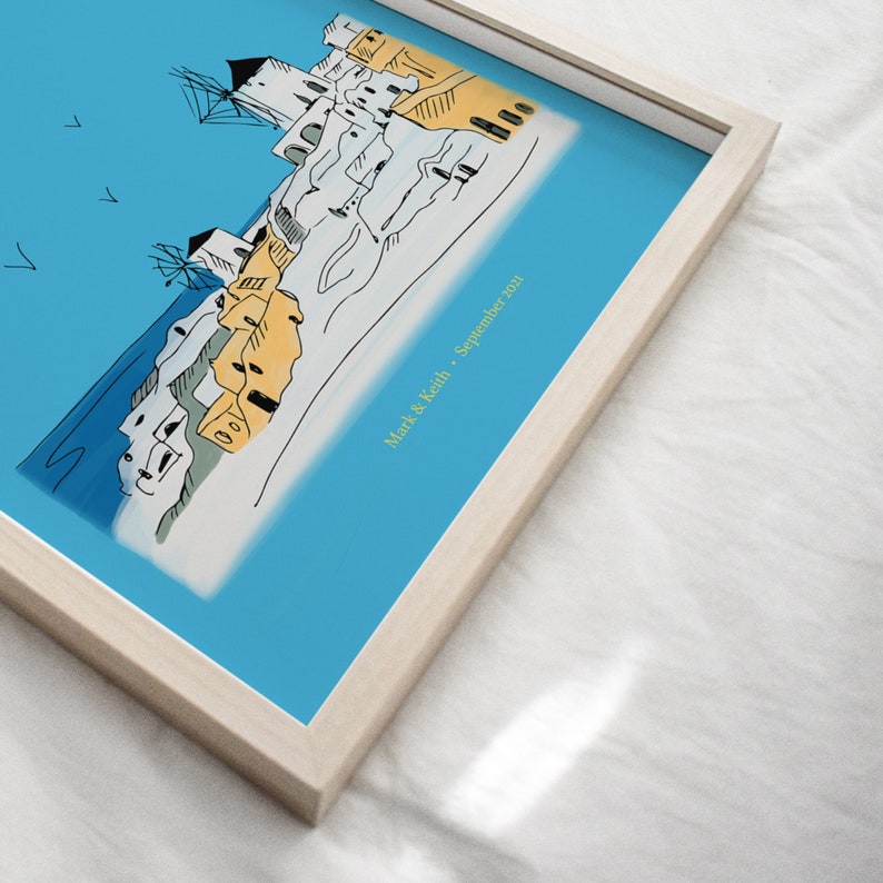 May include: A framed illustration of a seaside town with white buildings and blue roofs. The sky is blue and there are birds flying in the air. The text "Mark & Keith - September 2021" is written in the bottom right corner of the image.