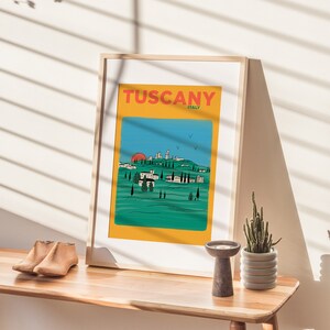 K&ouml;nnte beinhalten: Ein gerahmter Druck mit gelbem Hintergrund und blauem Himmel, auf dem eine rote Sonne &uuml;ber einer gr&uuml;nen Landschaft mit einer kleinen Stadt in der Ferne untergeht. Der Druck zeigt den Text "Tuscany, Italy" in roten und wei&szlig;en Buchstaben.