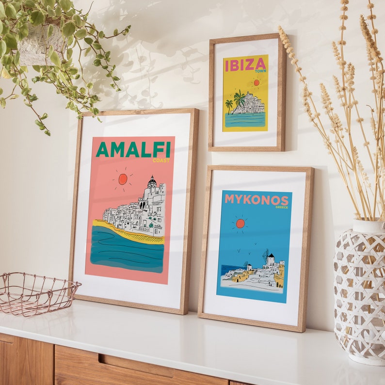 K&ouml;nnte beinhalten: Drei gerahmte Illustrationen beliebter Reiseziele. Die obere Illustration ist gelb mit dem Text "IBIZA TOWN" und einer Darstellung einer K&uuml;stenstadt. Die mittlere Illustration ist rosa mit dem Text "AMALFI COAST" und einer Darstellung einer K&uuml;stenstadt. Die untere Illustration ist blau mit dem Text "MYKONOS GREECE" und einer Darstellung einer K&uuml;stenstadt.