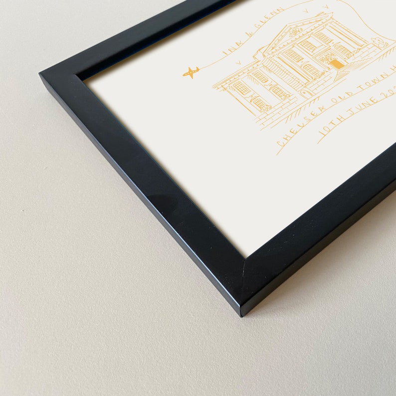 May include: A black picture frame with a white mount and a gold illustration of a building with the text "Chelsea Old Town Hall 10th June 2022" and "Ink & Glenn" above the building.