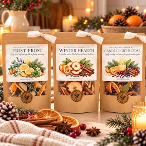 May include: Three kraft paper pouches of botanical simmer kits labeled First Frost, Winter Hearth, and Candlelight & Cedar. Each pouch features a clear window displaying dried fruit, spices, and herbs, topped with a white fabric ribbon tie.