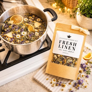May include: A stainless steel pot on a stovetop simmers with water, orange slices, and flowers. A kraft paper bag labeled "Fresh Linen" with citrus, herbal, and soft floral notes sits nearby. The bag is tied with a white ribbon.