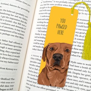 May include: Yellow bookmark with a brown dog illustration and the text "You Pawsed Here". The bookmark has a yellow tassel.