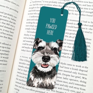 May include: Teal blue bookmark featuring a white and grey illustration of a miniature schnauzer dog. The bookmark has the text "You Pawsed Here" in white.