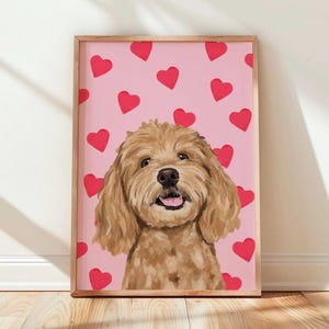 May include: A framed digital illustration of a golden-brown doodle dog with floppy ears and an open mouth, set against a light pink background patterned with numerous solid red hearts. The artwork is enclosed in a simple, light-toned wooden frame.
