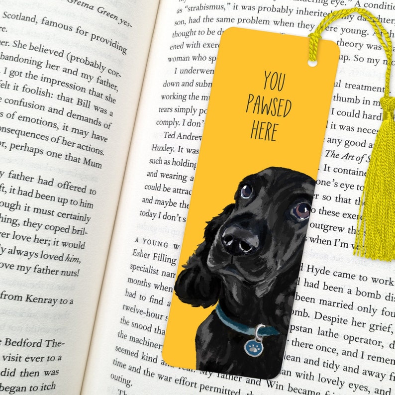 May include: Yellow bookmark with a black and white illustration of a dog's head. The bookmark has the text "You Pawsed Here" on it.