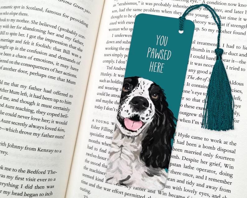 May include: Teal blue bookmark with a black and white illustration of a dog with the text "You Pawsed Here".