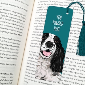 May include: Teal blue bookmark with a white and black illustration of a dog's head. The bookmark has the text "You Pawsed Here" in white.