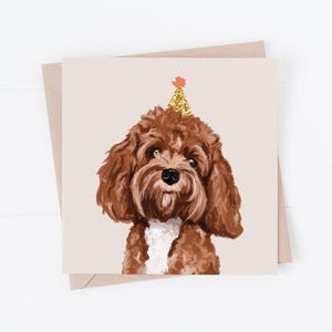 May include: A greeting card featuring a brown dog with a gold party hat and a white chest. The dog is centered on a beige background, with a brown envelope behind the card. The card is square.