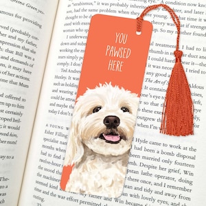 Könnte beinhalten: Ein weißer Hund mit rosa Nase und Zunge ist auf einem leuchtend orangefarbenen Lesezeichen abgebildet. Das Lesezeichen trägt den Text "You Pawsed Here" in weißen Buchstaben.