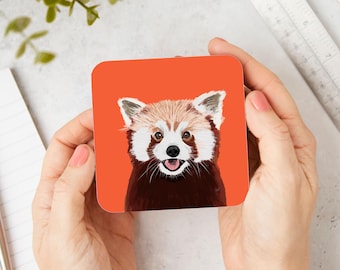 May include: A red panda with a white face and chest is looking directly at the camera. The red panda is on a bright orange background.