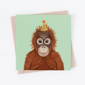 May include: A birthday card featuring a cartoon orangutan wearing a gold glitter party hat with an orange star on top. The orangutan has a light brown face and a light green background.
