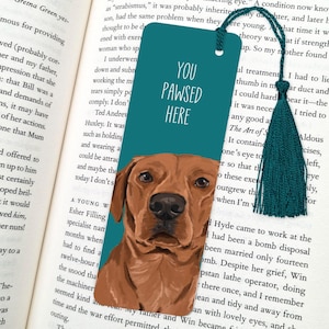 May include: Teal blue bookmark with a brown dog illustration and the text "You Pawsed Here". The bookmark has a teal tassel.