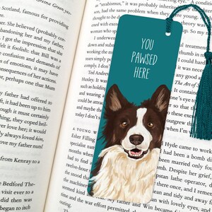 Pode incluir: Marca-p&aacute;ginas azul turquesa com uma ilustra&ccedil;&atilde;o de um c&atilde;o border collie branco. O marca-p&aacute;ginas tem o texto "You Pawsed Here" em branco.