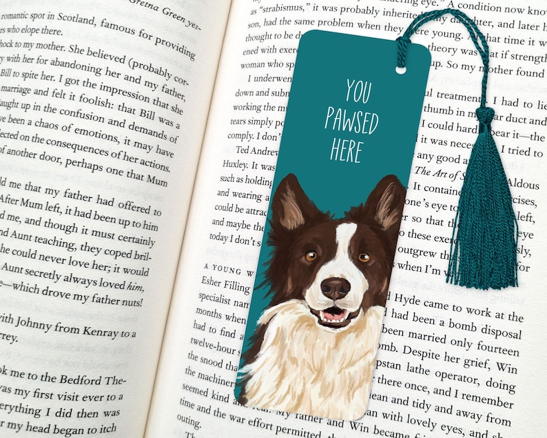 Pode incluir: Marca-p&aacute;ginas azul turquesa com uma ilustra&ccedil;&atilde;o de um c&atilde;o border collie branco. O marca-p&aacute;ginas tem o texto "You Pawsed Here" em branco.