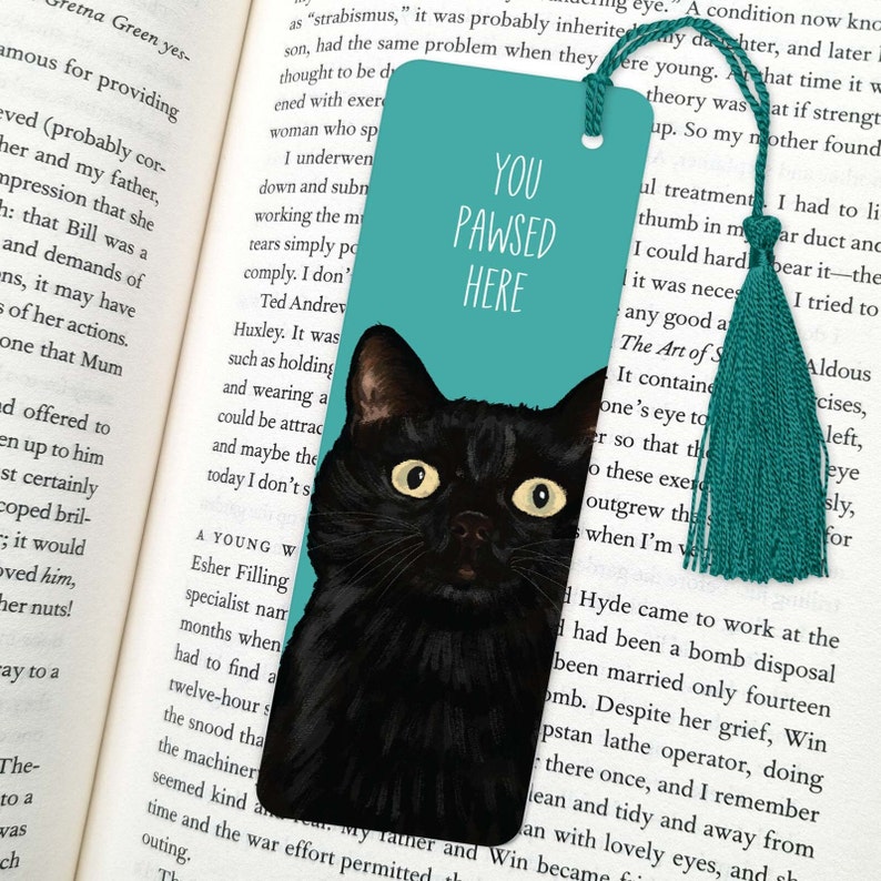 Peut inclure: Un marque-page bleu turquoise avec une illustration de chat noir et le texte "You Pawsed Here".