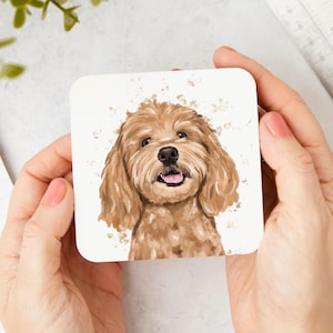 May include: A square coaster featuring a watercolour-style illustration of a golden-brown dog with floppy ears, a black nose, and an open mouth showing a pink tongue, set against a plain white background with subtle light brown paint splatters.