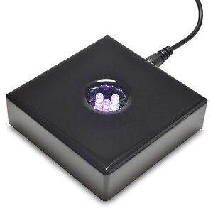 May include: A black square base with a circular platform on top. The platform has multiple small, colorful LED lights that illuminate the base.