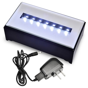 May include: A black rectangular display case with a glass top and a row of white LED lights. The case is illuminated from below and comes with a black power adapter and a cord.