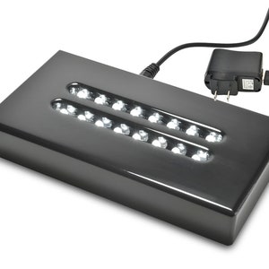 May include: A black rectangular display stand with a built-in LED light strip. The stand has two rows of white LED lights and is powered by a black AC adapter.