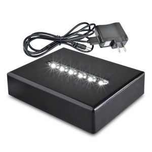 May include: A black rectangular display base with a row of white LED lights. The base is connected to a black power adapter with a cord.