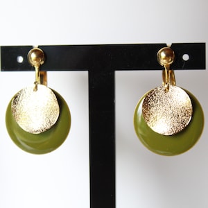 Può includere: Un paio di orecchini a clip dorati e verde oliva con un design rotondo. Gli orecchini presentano un cerchio dorato più piccolo sovrapposto a un cerchio verde oliva più grande.