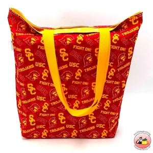 May include: A red and yellow tote bag with the words "USC Trojans" and "Fight On!" repeated on the fabric. The bag has two yellow straps.