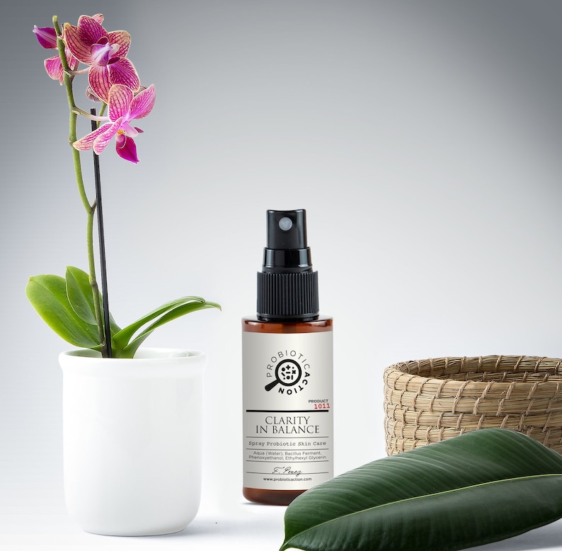 A close-up of a white spray bottle with a green label labeled "Clarity In Balance Probiotic Spray for Skin."