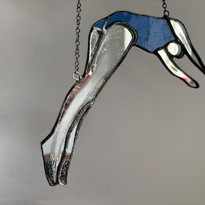 Może przedstawiać: Szklana ozdoba przedstawiająca osobę w niebieskim stroju kąpielowym, która nurkuje głową naprzód do wody. Ozdoba jest zawieszona na czarnym łańcuchu.