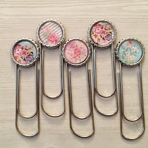 May include: Set of six silver paper clips with floral designs. Each clip features a different floral pattern in shades of pink, blue, and white.