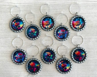 May include: Set of 10 wine glass charms featuring a colorful rose design on a black background. Each charm is attached to a silver ring.