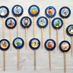 May include: A set of 15 blue and white cupcake toppers featuring characters from the Toy Story movie franchise. The toppers include Woody, Buzz Lightyear, Jessie, Mr. Potato Head, Rex, Slinky Dog, Hamm, Bo Peep, and the green alien. The toppers are perfect for a Toy Story themed party.