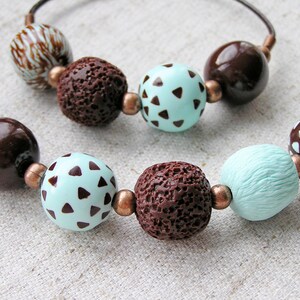 Op de afbeelding: Een bruine en turquoise kralenketting met bruine en witte gepatroneerde kralen. De ketting is gemaakt van verschillende materialen, waaronder hout, lavastenen en polymer clay.