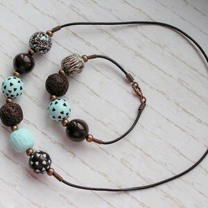 Op de afbeelding: Een ketting van bruin lederen koord met een bijpassende armband. De ketting en armband zijn versierd met bruin, blauw en wit gepatroneerde kralen.