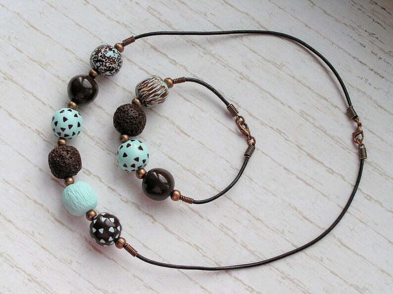 Op de afbeelding: Een ketting van bruin lederen koord met een bijpassende armband. De ketting en armband zijn versierd met bruin, blauw en wit gepatroneerde kralen.