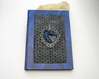 May include: A blue leather-bound journal with a black brick pattern and a silver dragon head ornament.
