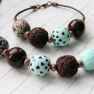 Op de afbeelding: Een bruine en turquoise kralenketting met bruine en witte kralen met patronen. De ketting is gemaakt van verschillende texturen, waaronder gladde, getextureerde en gepatroneerde kralen.