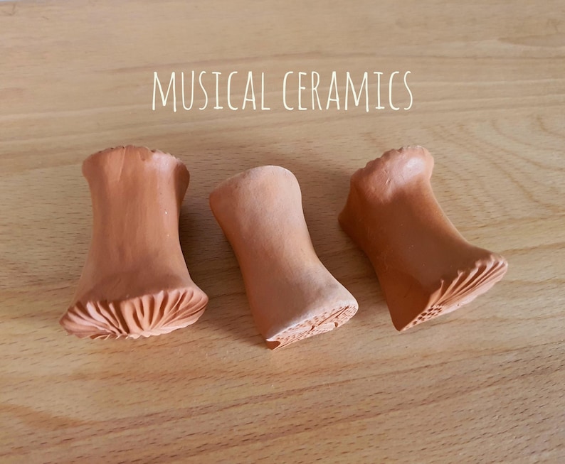 May include: Three terracotta-coloured ceramic objects with flared ends and textured bases, arranged in a row. The text MUSICAL CERAMICS is printed in white above the objects. Each piece has a smooth, cylindrical body that widens at both ends.