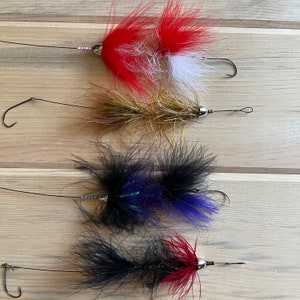 May include: Four different fly fishing lures with various colours and feather patterns. The lures are tied with red, white, gold, black and blue feathers.