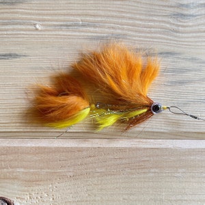 May include: A bright orange and yellow fly fishing lure with a brown and silver body and a single bead.