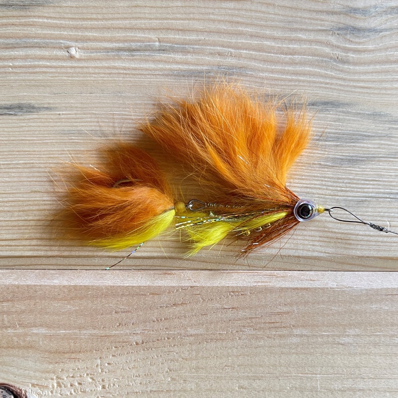 May include: A bright orange and yellow fly fishing lure with a brown and silver body and a single bead.